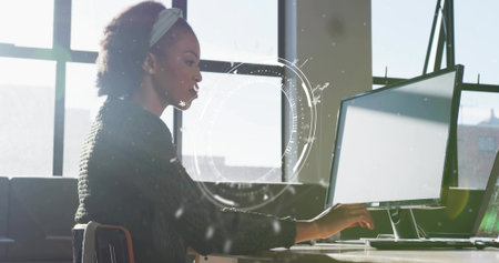 Analyzing woman wearing sweater at desk in office, viewing monitors with translucent UI overlay. Technology, professional, modern, productivity, innovation, workspace, focusの写真素材