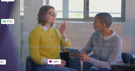 Woman wearing sweater speaking to coworker in glass office, with tablet social media icons....