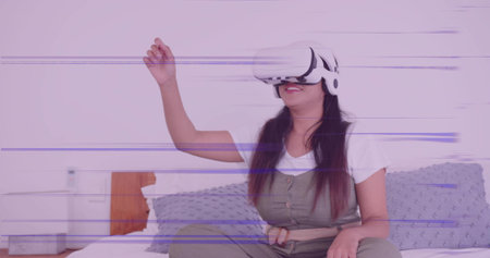 Woman wearing olive jumpsuit and headset experiencing virtual reality on bed, with white device....