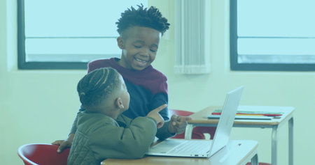 Collaborating children in green puffer jacket viewing silver laptop in classroom, with red chairs....