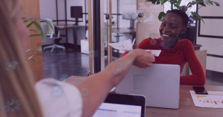 Colleagues exchanging printed reports in red white tops in open-plan office with laptop, copy space....