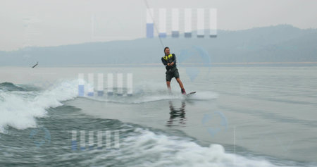 Gliding man wearing neon life vest on wakeboard across lake, gripping tow rope amid boat wake....