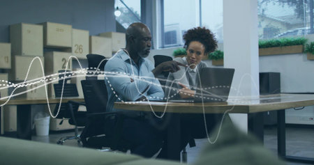 Collaborating professionals in button-down and gray blazer pointing at laptop in modern office. Corporate, teamwork, modern, professional, workspace, productivity, innovationの写真素材