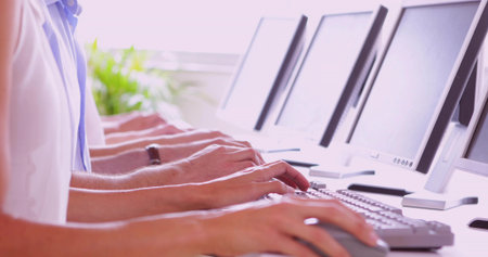 Office workers wearing polo shirts typing on keyboards at office desk, with monitors and plant. Collaboration, productivity, modern, ergonomic, technology, workspace, teamworkの写真素材