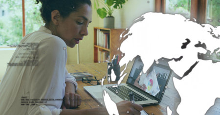 Leaning mature woman writing in notepad at home office desk, with laptop and world map overlay....