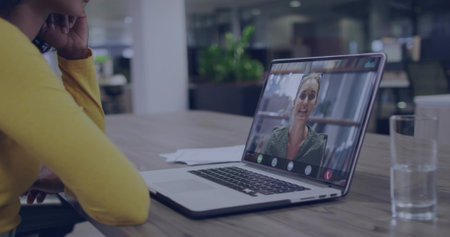 Viewing colleague on laptop, woman in sweater sitting at office with papers, water glass, plants. Professional, collaboration, modernity, communication, workspace, productivity, technologyの写真素材