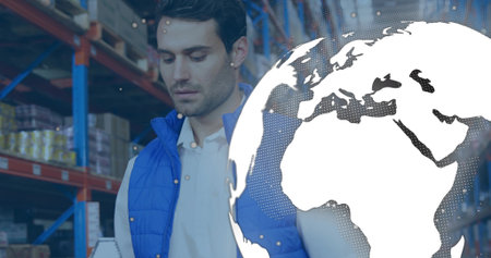 Reviewing inventory worker wearing blue vest in warehouse aisle with stacked boxes, globe overlay. Industrial, logistics, supply chain, inventory, distribution, warehouse, arrangementの写真素材