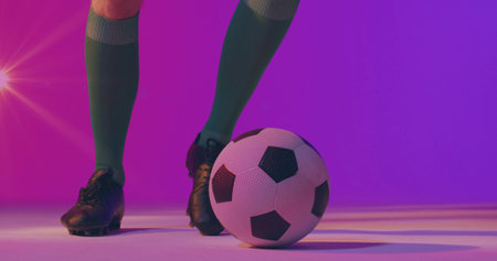 Standing player legs wearing green socks, black cleats in pink-purple studio, with soccer ball....
