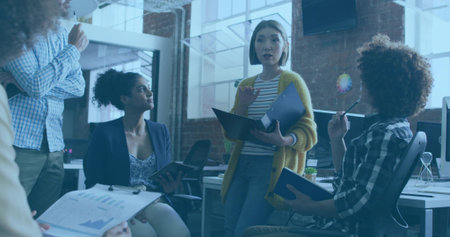 Leading woman wearing cardigan presenting folder in loft, with notebooks, color disc, laptop....