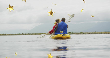 Paddling couple wearing red jacket, blue vest in yellow kayak crossing calm lake. Adventure,...