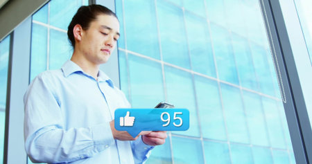 Man wearing shirt and pants reading smartphone screen beside office window, with thumbs-up icon 95....