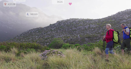 Hiking couple traversing mountain trail in red jacket with boots, poles and backpacks, copy space. Adventure, exploration, outdoor, landscape, fitness, endurance, natureの写真素材