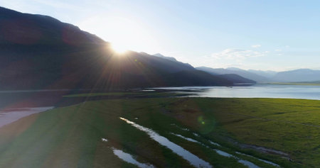 Shining central mountain ridge radiating sunbeams across marshy valley, with calm lake waters. Scenic, landscape, wilderness, tranquility, dawn, serenity, naturalの写真素材