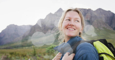 Smiling hiker holding neon yellow-green backpack, gazing in mountains with blue jacket, copy space....