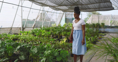 Browsing woman wearing white T-shirt, skirt, shoulder bag in plant nursery with plants, copy space. Garden, foliage, horticulture, tranquility, eco-friendly, natural, growthの写真素材