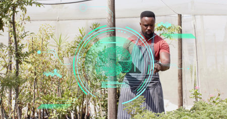 Inspecting African American gardener tending plants in plant nursery with smartwatch AR, copy space. Horticulture, greenery, technology, modern, landscape, sustainable, professionalの写真素材