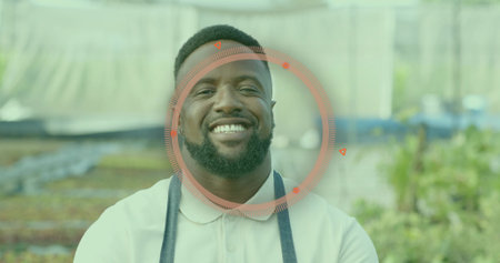 Smiling mid adult male gardener tending seedling trays in greenhouse, with apron and metal benches. Horticulturist, sustainable, vibrant, eco-friendly, growth, cultivation, agriculturalの写真素材