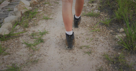 Walking person wearing black boots and white crew socks on gravel trail with grass, wooden boards....