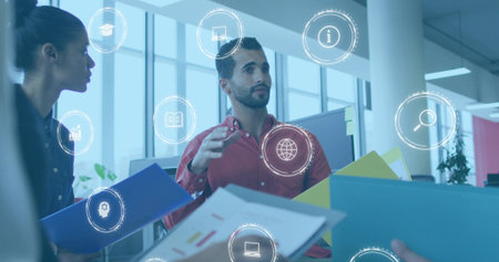 Coworkers gesturing and discussing in modern office in business attire, with binders, digital icons. Collaboration, teamwork, innovation, communication, corporate, professional, brainstormingの写真素材