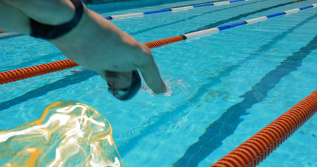 Diving athletic male swimmer entering competition pool, with red white blue lane ropes, copy space. Athlete, aquatic, minimalist, sports, fitness, outdoor, hydrationの写真素材