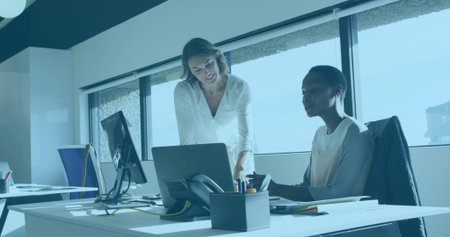 Collaborating professional women pointing laptop screen in bright modern office, with office phone....