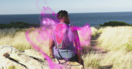Sitting male hiker facing sea horizon on coastal bluff, with red-gray daypack and purple mist. Nature, adventure, exploration, wilderness, serenity, outdoor, tranquilityの写真素材