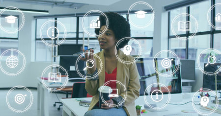 Woman wearing tan blazer interacting with analytics icons in office, holding pen and coffee mug. Technology, innovation, professional, workspace, digital, collaboration, abstractの写真素材