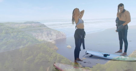 Standing duo adjusting hair and holding wetsuit jackets at beach, with red and white surfboards....