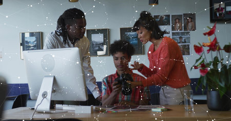 Reviewing professionals examining DSLR camera captures at studio desk with monitor and plant. Collaboration, innovation, creative process, photography, digital arts, workspace, teamworkの写真素材