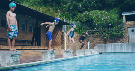 Preparing four children wearing swim caps and goggles balancing on diving blocks at pool deck. Children, aquatic sports, outdoor, leisure, vibrant, teamwork, youthの写真素材