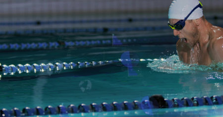 Swimmer emerging at pool swimming past lane dividers, in white swim cap, dark goggles, copy space. Athlete, aquatic, training, fitness, competition, sport, recreationの写真素材