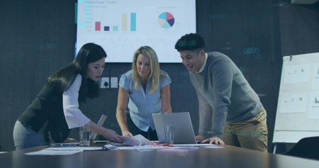 Collaborating three colleagues analyzing sales in boardroom, with laptop computer, monitor display. Business, teamwork, analytics, data, corporate, strategy, officeの写真素材