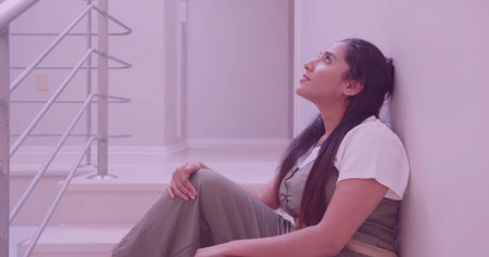 Leaning Indian woman sitting on stair landing by pale wall, with white steps silver metal banister....