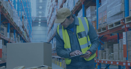Leaning warehouse worker inspecting inventory using tablet in long aisle, with boxes and racks....