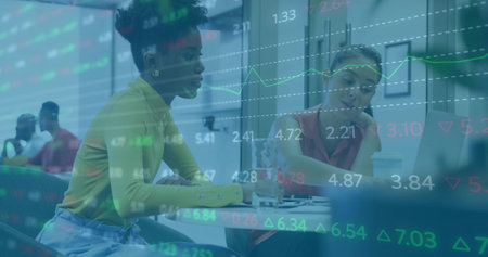 Two businesswomen reviewing printed charts in meeting room with laptop coffee cup and data overlay. Professional, collaboration, modern, analytic, corporate, workspace, dynamicの写真素材