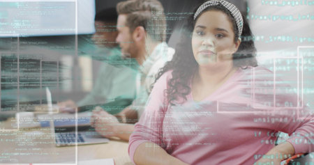 Woman wearing pink sweater and headband reviewing projected code in office, with laptops. Collaboration, innovation, modernity, teamwork, technology, creativity, productivityの写真素材