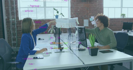 Reaching businesswoman passing printed chart to colleague over divider in office, with monitors....