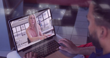 Holding laptop, man wearing polo viewing remote call in shared office with keyboard and overlay....
