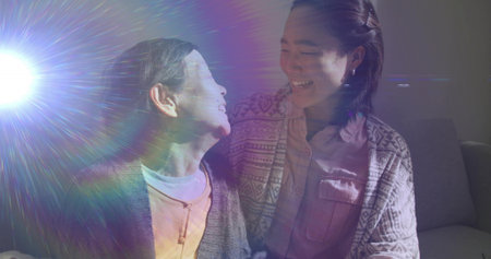 Sharing smiles grandmother and granddaughter sitting on sofa in living room, with lens flare light....