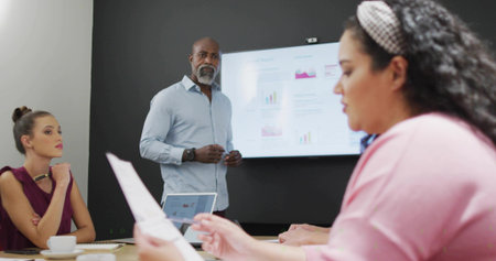 Presenting senior manager pointing at display screen in meeting room, with laptop and printed pages. Collaboration, teamwork, agenda, brainstorming, innovation, productivity, professionalの写真素材