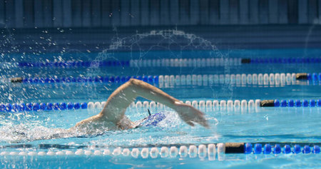Female swimmer performing front crawl in racing pool, wearing swim cap and goggles with lane ropes. Athlete, aquatic, sports, training, competition, movement, waterの写真素材