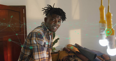 Leaning craftsman wearing plaid shirt arranging leather hides in studio, with hanging bulbs. Artisan, leatherwork, craftsmanship, creative studio, handmade, rustic, designの写真素材