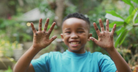 Smiling African American child holding dirt-covered hands up in backyard garden, with potted shrubs. Joyful, youthful, outdoor, nature, innocence, growth, vibrantの写真素材