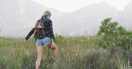 Hiking woman walking through field to misty foothills, with backpack water bottle and hiking boots....