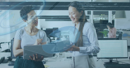 Collaborating women reviewing documents in office with data graphics, laptop and folder. Collaboration, teamwork, productivity, modern, corporate, technology, communicationの写真素材