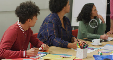 Collaborating colleagues taking notes at wooden table in meeting room, with colored pencils, mug....