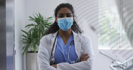 Standing doctor wearing blue scrubs, white lab coat and mask in hospital corridor, with stethoscope. Medical, healthcare, professional, clinical, hospital, modern, clinical environmentの写真素材