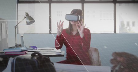 Reaching out worker wearing red dress VR headset at office, engaging VR interface with laptop....