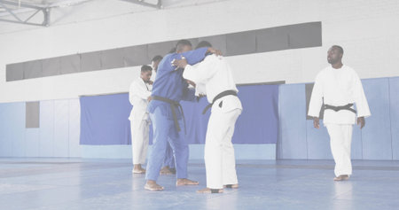 Grappling pair locking in clinch on dojo blue mats, with judo gis and black belts. Martialarts, competition, training, athletic, flexibility, discipline, teamworkの写真素材