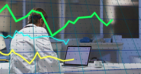 Male doctor in lab coat analyzing data on laptop in clinic, with coffee cup, stethoscope, graphs....